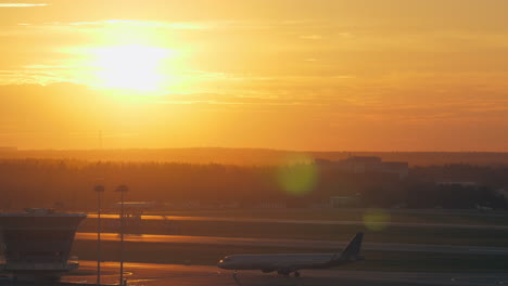 Vista-Del-Aeropuerto-Con-Avión-En-Movimiento-Al-Atardecer-Dorado.