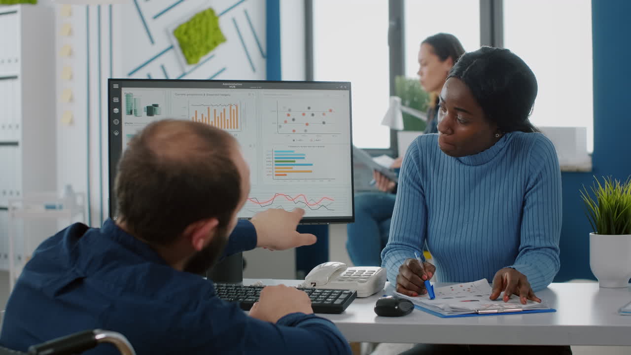 Invalid entrepreneur in wheelchair and african employee working at financial project