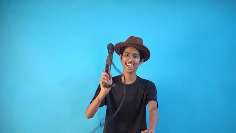 Fun-young-Indian-boy-in-basic-black-t-shirt-isolated-on-blue-background-studio-and-playing-with-long-whip