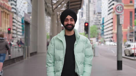 punjabi sikh man looks and smiles at camera while standing in the sidewalk of street