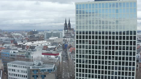 Descending-shot-along-modern-high-rise-office-building-with-large-glossy-windows-reflecting-sky-and-building-in-urban-neighbourhood.-Cologne,-Germany