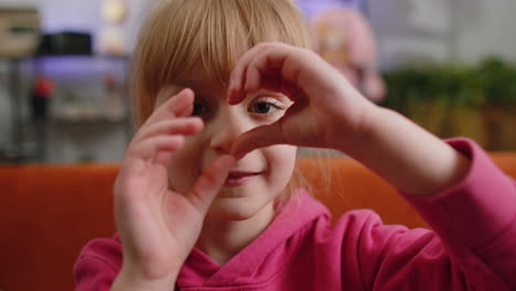 Young-child-kid-girl-makes-symbol-of-love,-showing-heart-sign-to-camera,-express-romantic-feelings