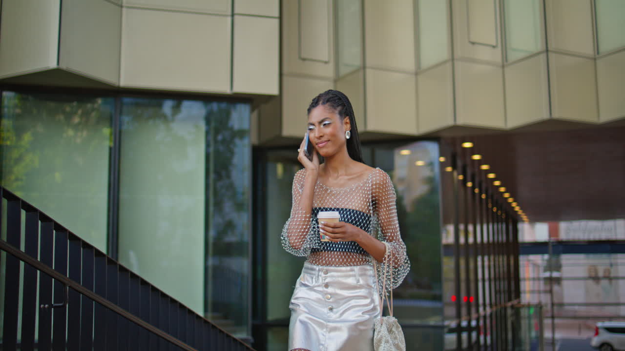 도시 거리에서 커피를 들고 있는 여성이 전화를 걸고 있습니다. 패션스타가 이야기하고 있습니다.