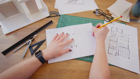 pov shot of female architect writing in notebook working in office on plans for new building