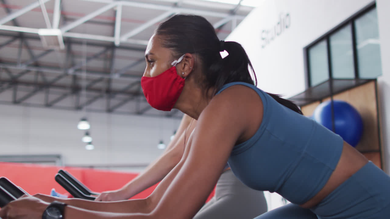 Diverse women wearing face masks exercising at gym
