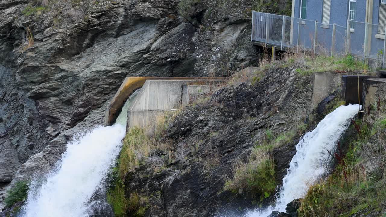 Water rushes from a hydroelectric station in Queenstown, New Zealand. The scene captures dynamic flow against rocky terrain