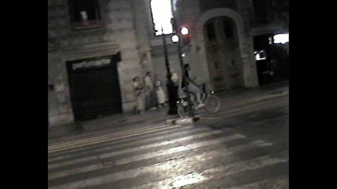 Night street scene with car, pedestrians, and bicycle