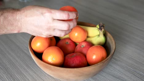 person taking clementine from fruits bowl placed on wooden table, nested sequence