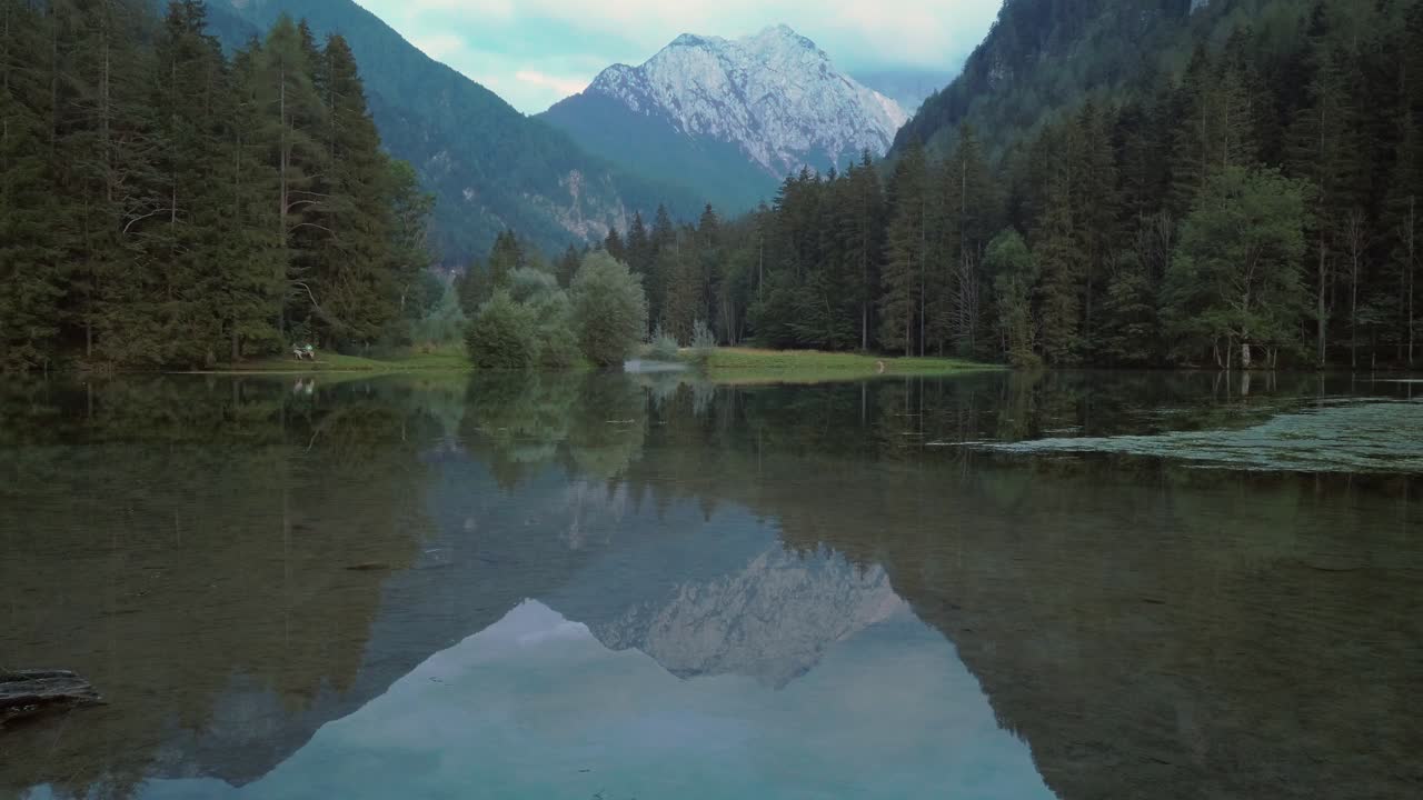 Alpine mountain range reflecting in lake Plansar or Plansarsko jezero in Jezersko, Slovenia in autumn, slow panning left to right
