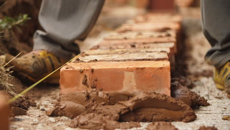 Primer-Plano-De-Un-Constructor-Africano-Colocando-Ladrillos-Sobre-Hormigón-Con-Mezcla-De-Cemento-Marrón