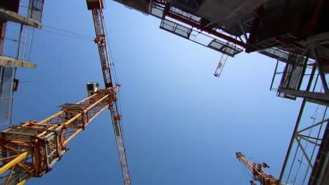 workers manage towering cranes at a bustling construction site on a sunny day. the project showcases modern urban architecture in progress, with visible structures reaching upward.