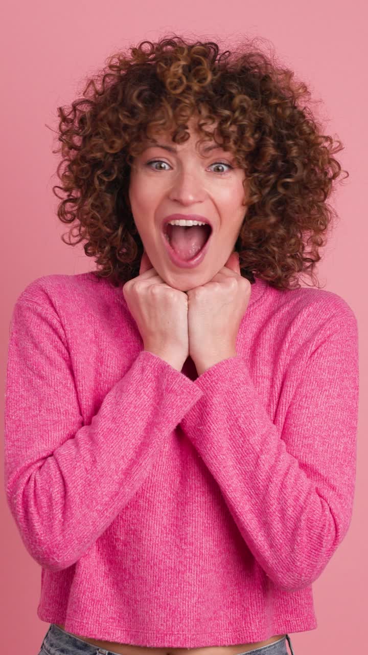 Stunned young woman standing with opened mouth on pink background. Vertical footage
