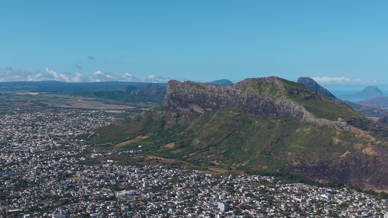 Aerial view of Beau Bassin–Rose Hill, Mauritius, featuring dramatic mountain ridges rising above the urban landscape under a clear tropical sky