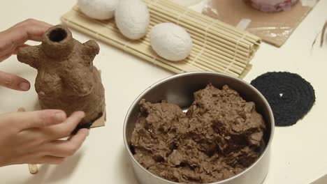 hands shaping paper air dry clay made of recycled egg carton beside a pottery piece on a crafting table, diy craft project
