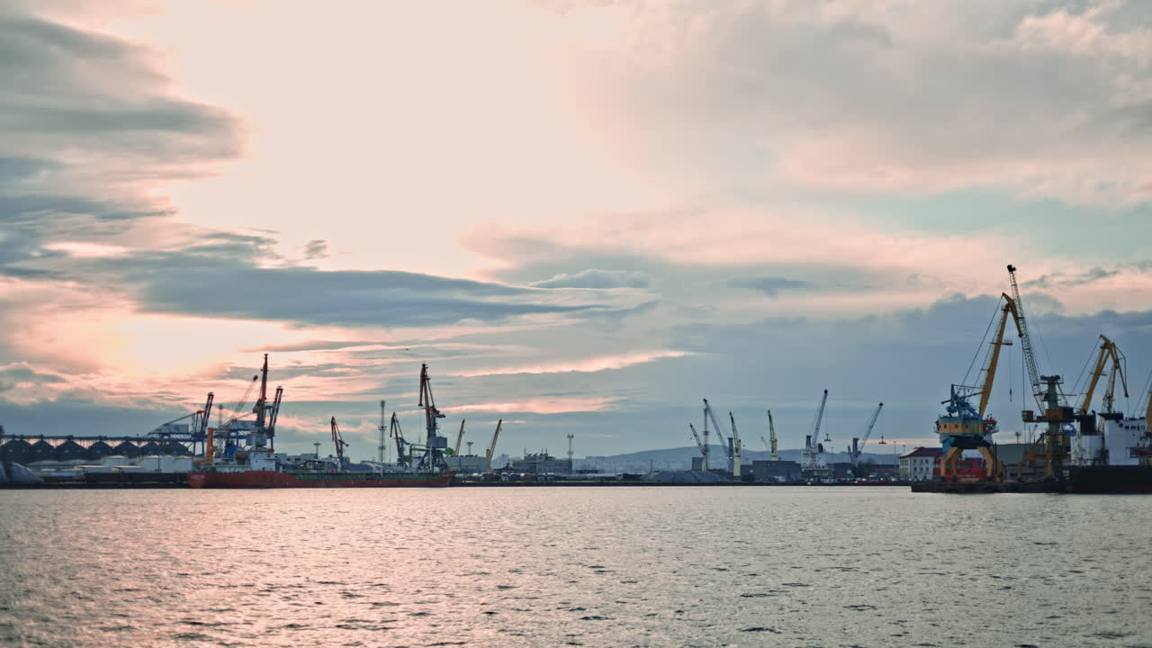 Ships and cranes work together at the busy harbor during sunset on a cloudy evening in a coastal city