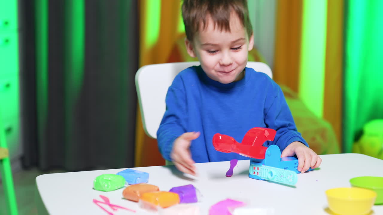 Toddler boy in blue sweater plays with molding machine. Happy kid absorbed by the game.