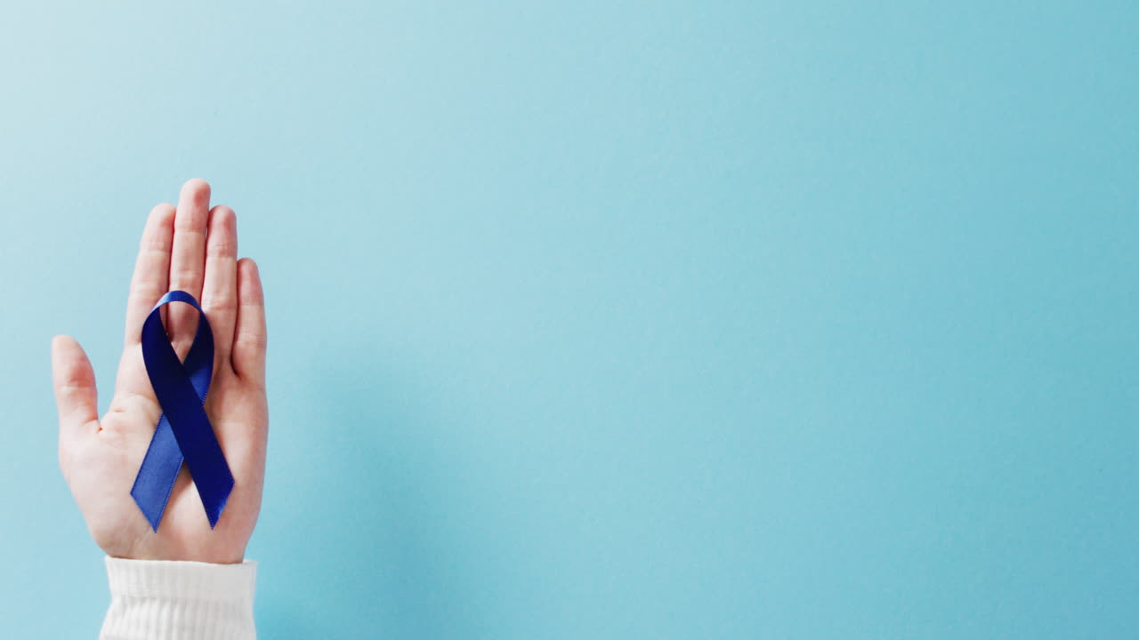 복사 공간과 함께 파란색 배경에 파란색 대장암 인식 리본을 들고 있는 손의 비디오