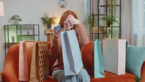 excited young caucasian woman with shopping bags receiving order sitting on sofa couch at home