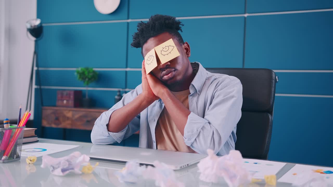 Funny lazy office worker napping at workplace covering eyes with sticky notes