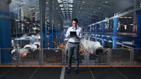 full body side view of an asian male professional worker standing with his tablet at the center of the wind turbine factory, typing on his tablet's keybaord with meditation