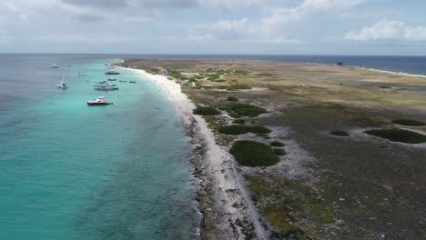 drone flying over coastal rocky coral shore with clear ocean water private island with boats ankered