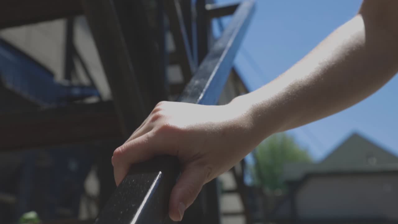 Hand Of A Man Holding On The Metal Railings While Walking Down The Stairs On A Sunny Day. - close up shot