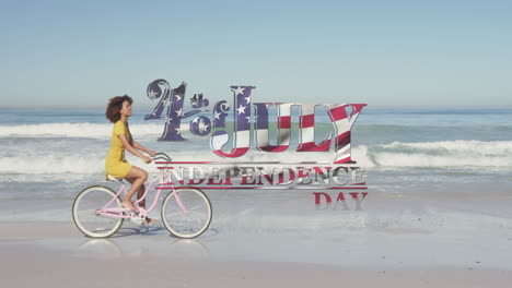 bandera estadounidense ondeando sobre el texto del día de la independencia contra la mujer montando en bicicleta en la playa