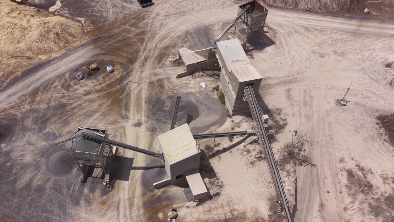 Overhead view of a sand and gravel quarry processing plant with conveyor belts, industrial crushers, and stockpiles of aggregate material on dry sandy terrain