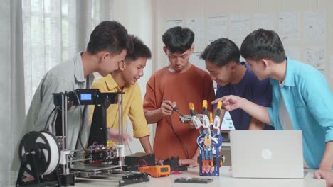 group of young asian boys with a cyborg hand and 3d printing fixing the circuit board while working on a laptop at home