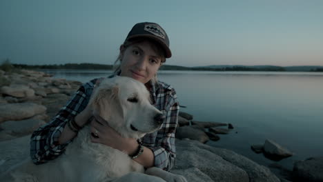 cheerful woman posing for camera with dog by lake