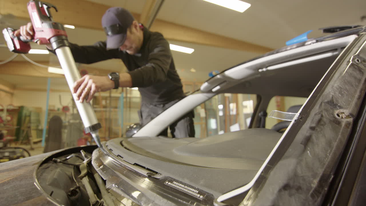 автомобильный стеклоремонтник наносит уретановый клей для установки нового лобового стекла