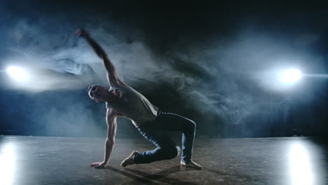 male dancer performs a stunt jump with a rotation back and a revolution in the scene in the smoke in the spotlight. modern ballet