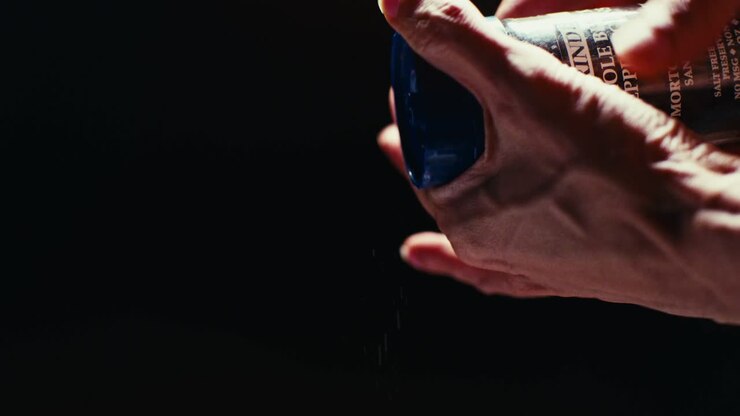 Mano dello chef che gira elegantemente un macinapepe nero su sfondo nero. Ripresa al rallentatore con illuminazione professionale da studio.