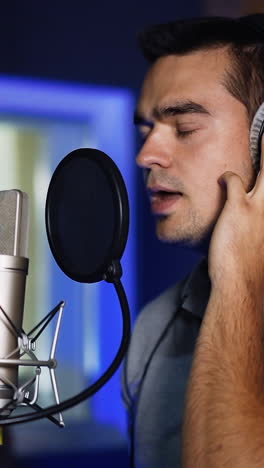 caucasian singer wearing headphones holding them with his hands sings in front of professional microphone. music studio song recording. vertical video