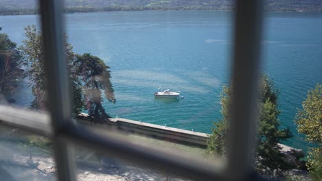 view of small motorboat from a window in annecy french alps, pan right shot