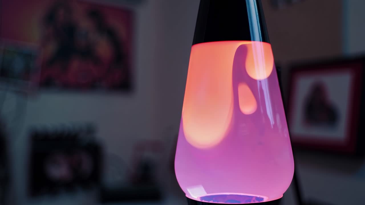Colorful lava lamp in motion, showcasing vibrant pink and orange wax blobs rising and falling, creating a mesmerizing visual flow in a cozy ambient setting