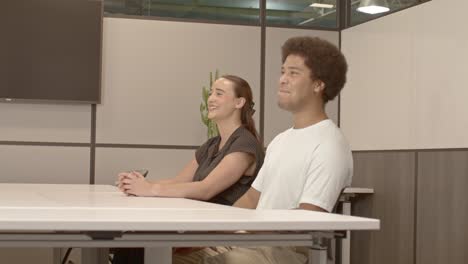 un hombre afroamericano de unos 20 años y una mujer caucásica de unos 20 anos hablando en una reunión de negocios con video moviéndose de izquierda a derecha con la puerta en primer plano