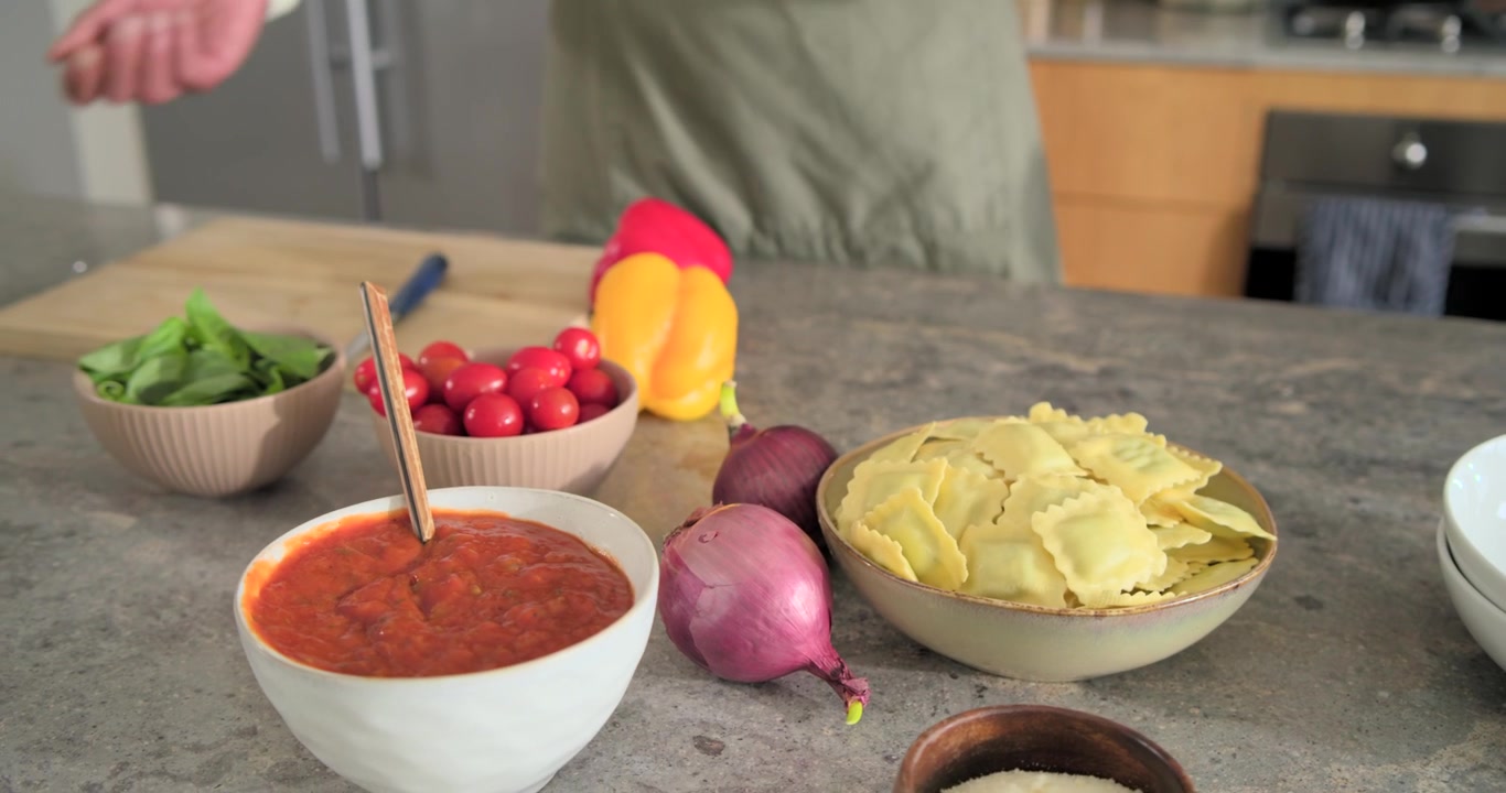 Vertical video: Draining water, cook with apron moving cherry tomatoes to bowl at sink for dinner