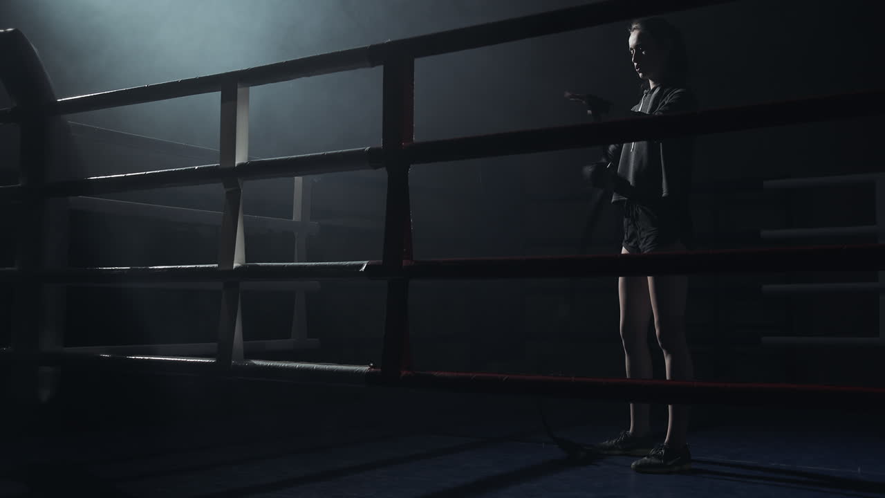 Female Boxer Prepares in a Dark Boxing Ring