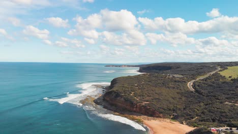 Aerial-view-of-coastal-landscape-of-Torquay-Bells-Beach-surrounded-by-lush-green-hills-that-rise-up-from-the-shoreline