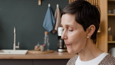 Mature woman tasting something with expressive facial reactions in a kitchen