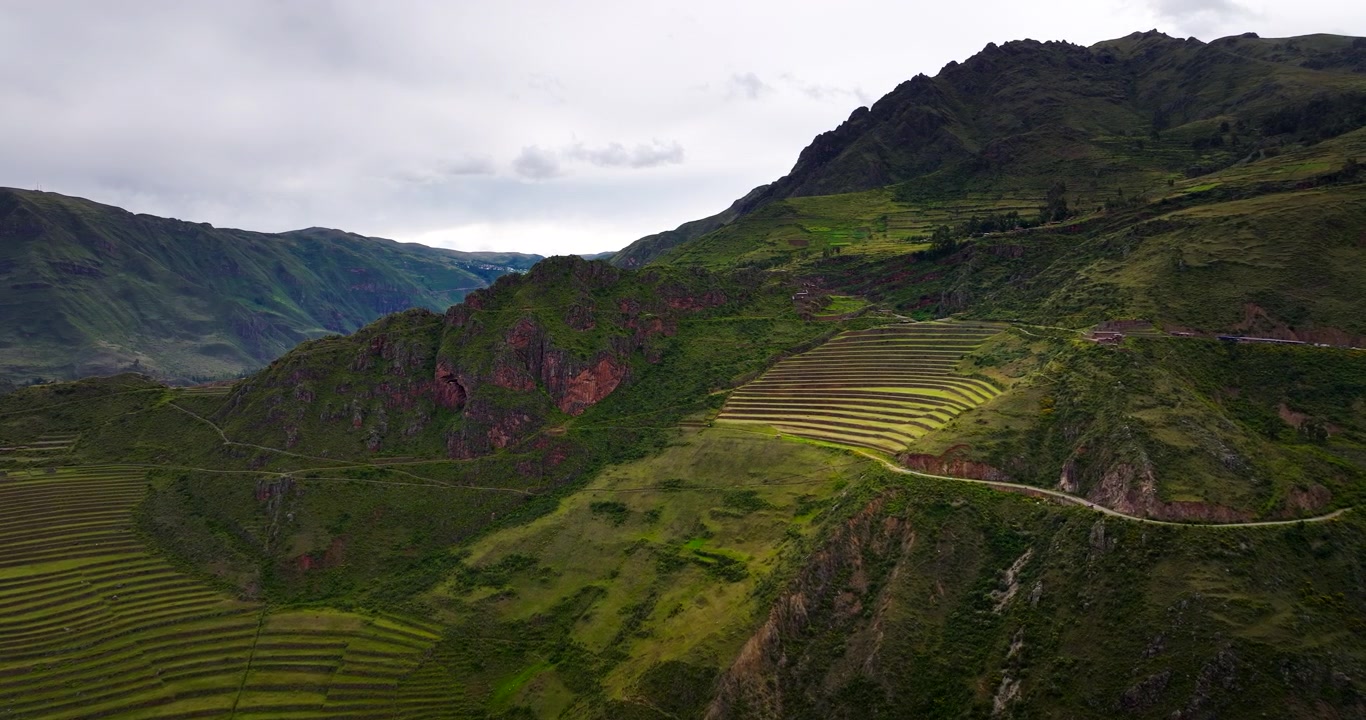 Paesaggio terrazzato Inca al Parque Arqueológico Pisac nella Valle Sacra, Perù, con pendii montani, opere di sterro archeologiche e una strada tortuosa, vista aerea.