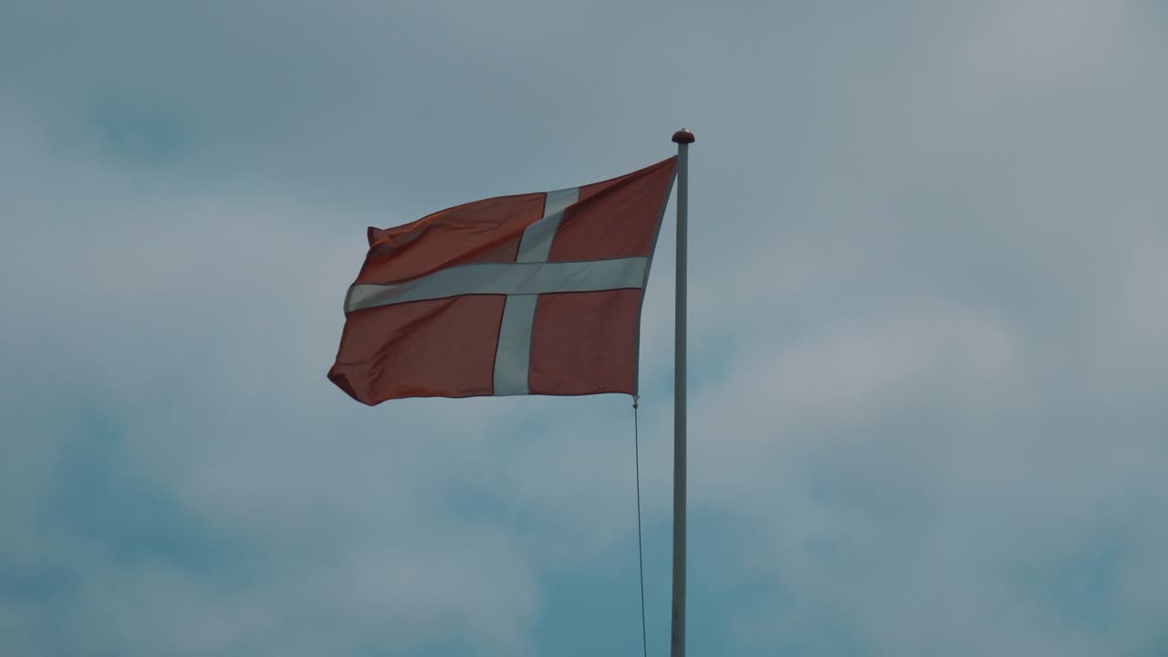 Danish national flag flutters in the wind with blue sky in background in slightly slow motion