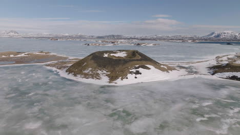 Drone-Shot-of-Volcanic-Crater-in-the-Middle-of-Frozen-Glacial-Lake-in-Landscape-of-Iceland