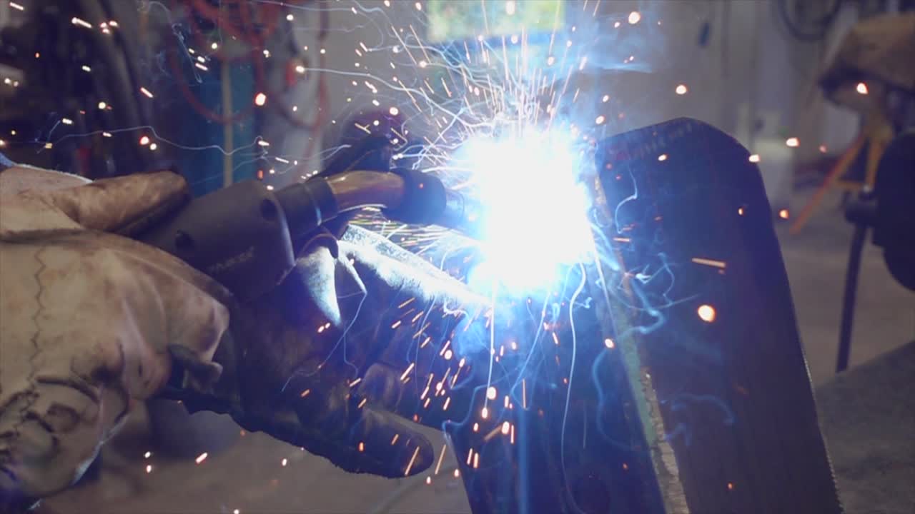 Gloved hands holding welding torch with bright sparks flying, steel craftsman