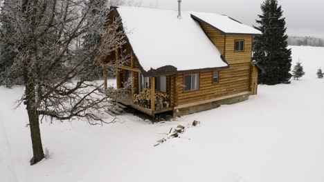 cierre el carro aéreo lento a la izquierda alrededor de una acogedora y cálida cabaña de troncos en un entorno invernal durante una ligera nevada