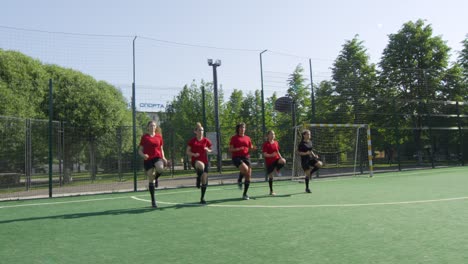 team of young female soccer players in uniform running on field together while training outdoors on sunny summer day