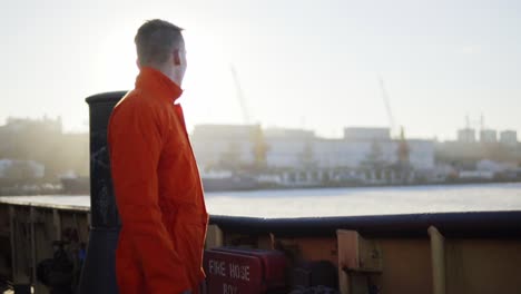 Trabajador-Portuario-Con-Uniforme-Naranja-Parado-Junto-Al-Tablero-Del-Barco-Y-Descansando.-Destello-De-Lente.-Camara-Lenta