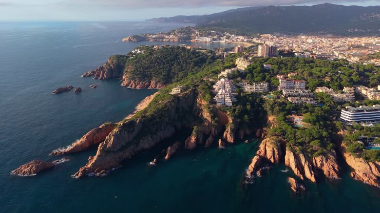 Stunning aerial perspective showing the rocky coastline and beautiful seaside town of sant feliu de guixols, with the s'agaro bay and beach in the background on the sunny costa brava