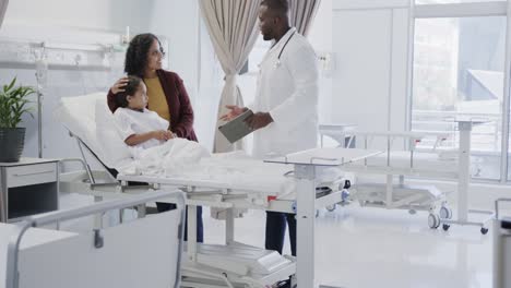 Worried-diverse-mother-with-her-sick-daughter-patient-talking-to-doctor-in-hospital-in-slow-motion